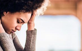 Eine Frau, die erschöpft den Kopf gesenkt hat und ihn mit der linken Hand abstützt
