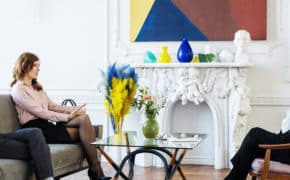 Mann und Frau sitzen auf einem Sofa, gegenüber sitzt eine Frau in einem Stuhl