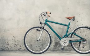 dunkelgrünes Retro Fahrrad mit altem braunen Sattel, etwa aus den 90ern, vor grauer Hauswand.