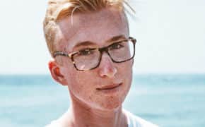 Junge mit Brille steht am Strand