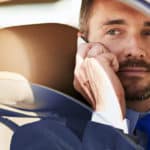 Mann sitzt mit Handy im Auto.