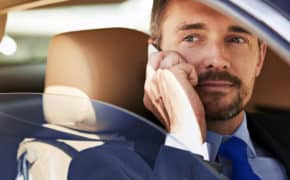 Mann sitzt mit Handy im Auto.