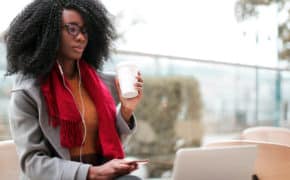 Frau schaut nachdenklich auf einen Laptop beim Kaffeetrinken.