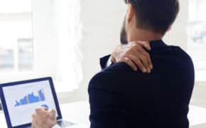 Mann sitzt am Laptop und fasst sich an den Rücken