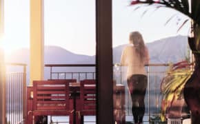 Frau steht auf Terasse und guckt in die Sonne