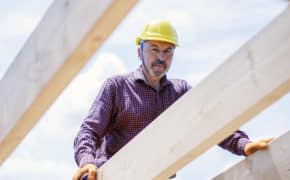 Mann mit Bauhelm steht auf Baustelle zwischen Dachbalken.