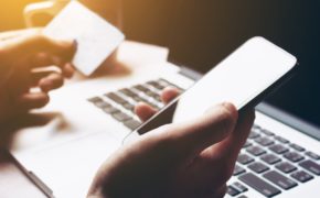 Frauenhände vor einem Laptop. In der einen Hand ein Smartphone, in der anderen Hand eine Kreditkarte. Internetshopping