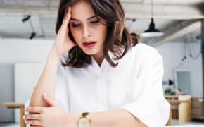 Frau sitzt am Arbeitsplatz und fasst sich an den Kopf.