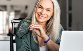Eine ältere Frau sitz lächelnd vor ihrem Laptop.
