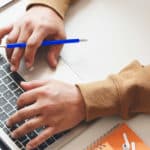 Person mit blauem Stift in der Hand benutzt einen Laptop