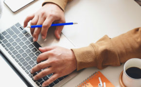 Person mit blauem Stift in der Hand benutzt einen Laptop