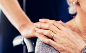 Ältere Frau im Rollstuhl hält die Hand ihres Kindes
