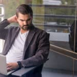 Mann sitzt mit Laptop auf seiner Terrasse.