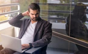 Mann sitzt mit Laptop auf seiner Terrasse.