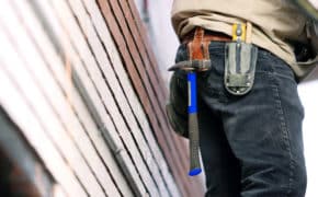 Mann auf Baustelle trägt Hammer.