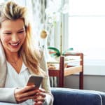 Blonde Frau schaut lachend auf ihr Samsung Smartphone