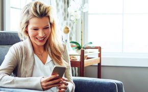 Blonde Frau schaut lachend auf ihr Samsung Smartphone