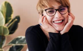Frau mit Brille hat Hände im Gesicht und lächelt