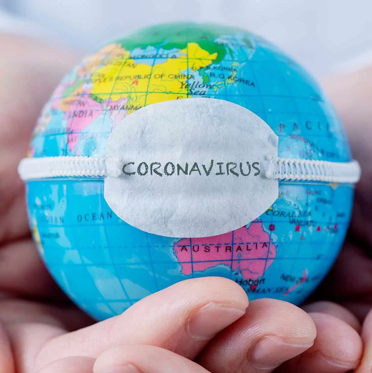 Hände, die einen Globus mit einer Atemmaske halten, auf der Coronavirus steht.