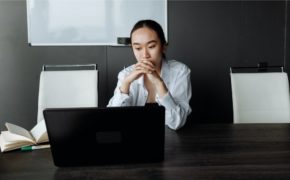 Frau sitzt an ihrem Schreibtisch und schaut nachdenklich auf den Laptop