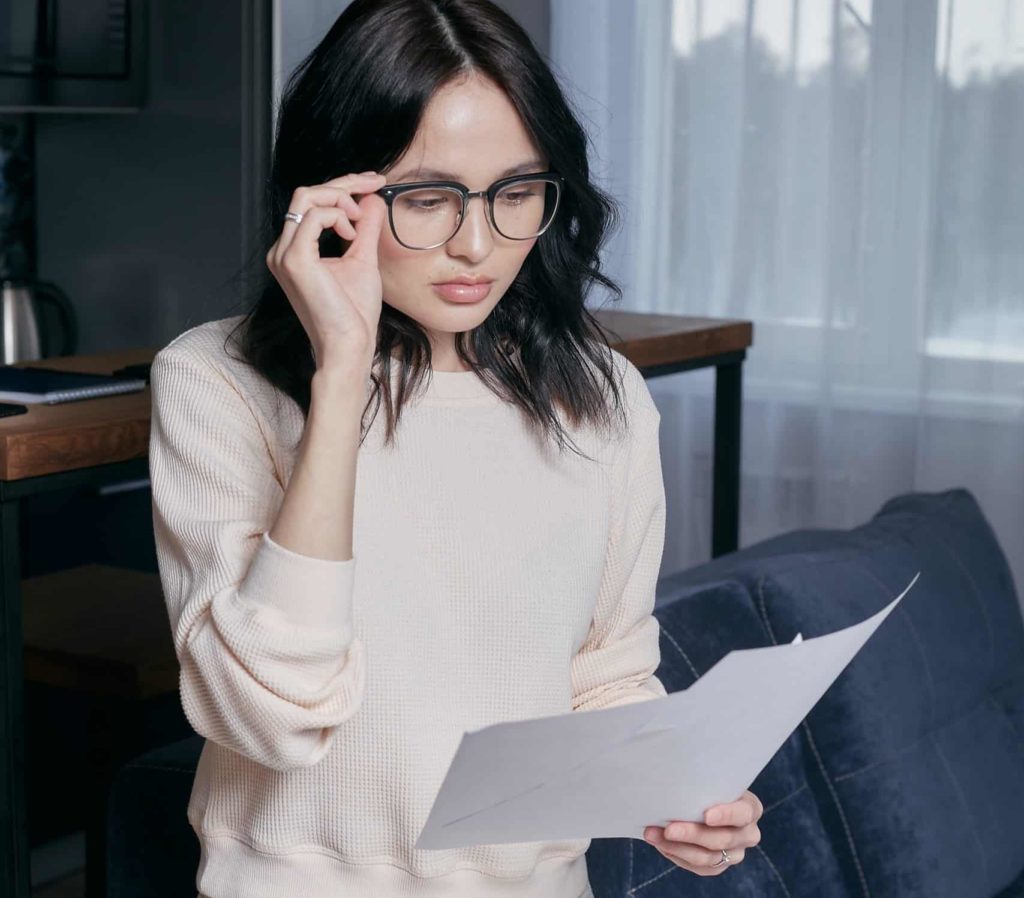 Eine Frau blickt durch ihre Brille skeptisch auf einen Rechnungsauszug