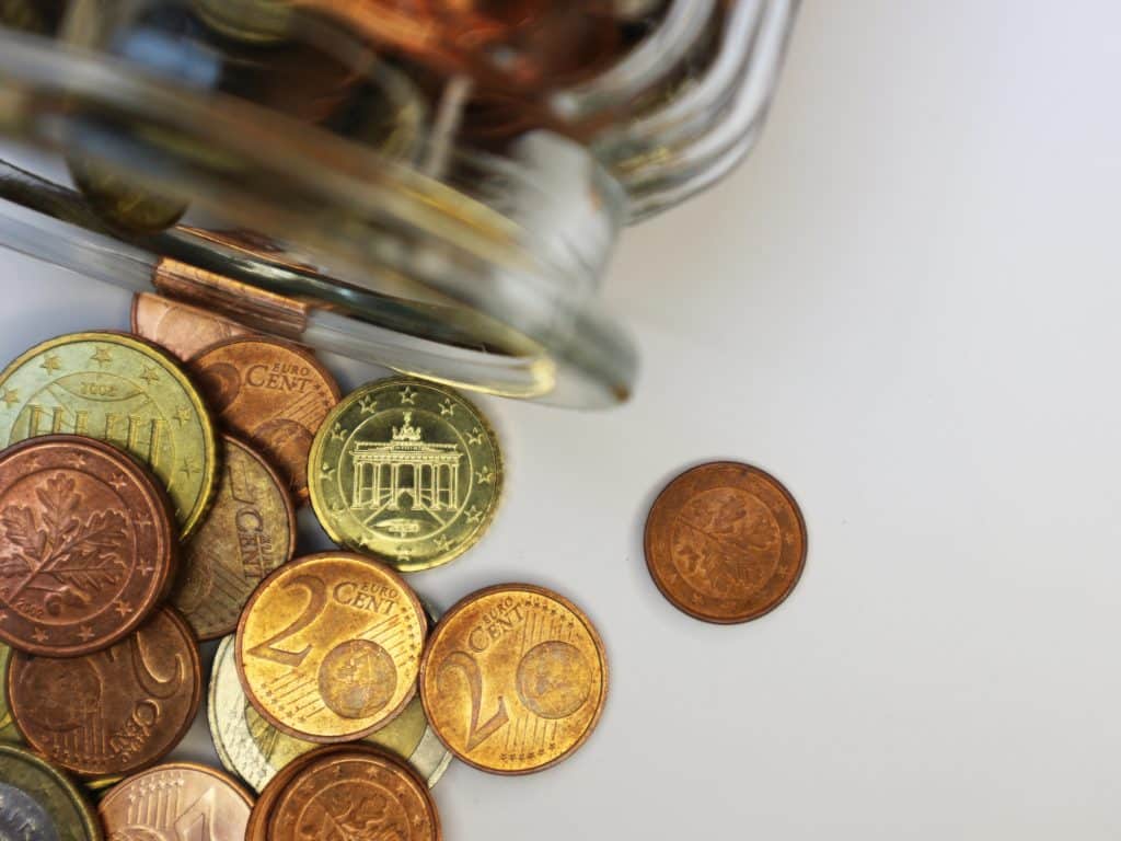 Ein Münzglas, aus dem sich Cent-Stücke auf einen Tisch ergießen. Studie von CLARK zeigt: Menschen in Deutschland setzen immer noch auf das Girokonto zum Geldsparen
